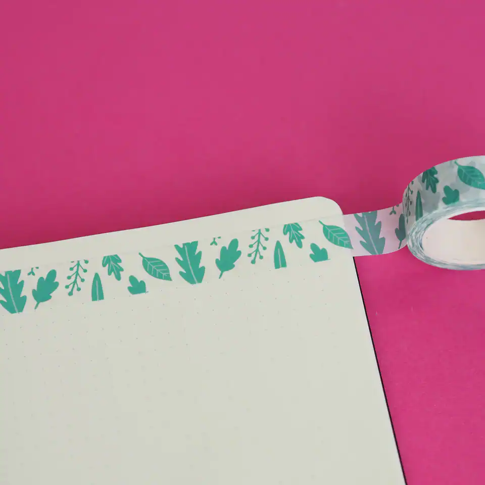 Colorful leaf-patterned washi tape on white paper against pink background, used for decorative crafts and stationery embellishments.
