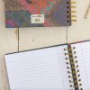 Colorful patterned planner and open spiral notebooks with gold accents on a rustic wooden surface, representing organization and creative planning at The Wraperie.