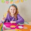 Colorful fruit-themed arts and crafts with a young girl smiling, working on citrus slice paper cutouts, showcasing creative activities at The Wraperie.