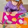 Colorful fruit-themed craft with a young girl coloring oranges and strawberries on vibrant paper, showcasing fun, creative activities for kids at The Wraperie.