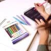 Bright colorful gel pens and weekly planner on white desk, organized stationery for working or studying, promotional image for The Wraperie and gift wrapping ideas, stationery supplies for office or school.