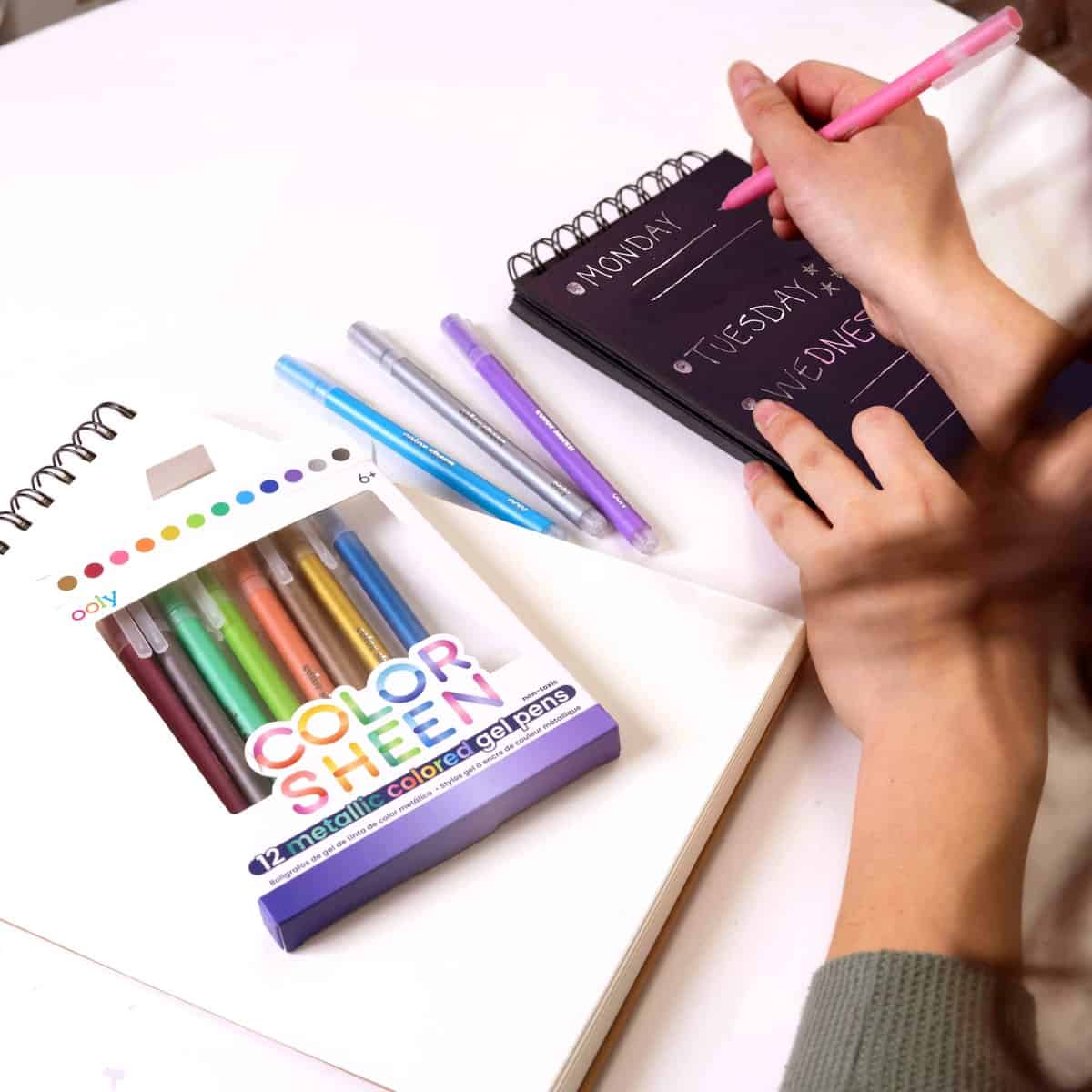 Bright colorful gel pens and weekly planner on white desk, organized stationery for working or studying, promotional image for The Wraperie and gift wrapping ideas, stationery supplies for office or school.